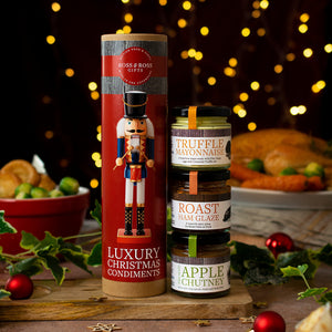 Two bottles of food products with decorative labels on a festive background with lights and food items.