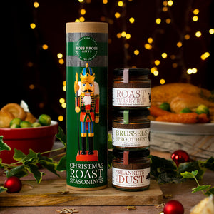 Two seasoning containers on a table with festive decorations and blurred lights in the background